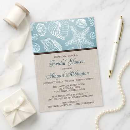 Rustic Beach Linen Seashell Bridal Shower Invitation shown on a marble surface with decorative items.