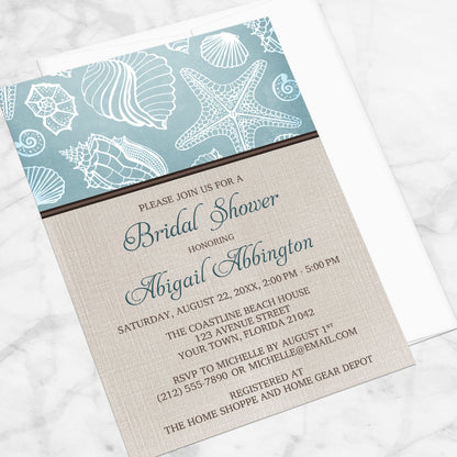 Rustic Beach Linen Seashell Bridal Shower Invitation shown at an angle on a marble surface with a white envelope.