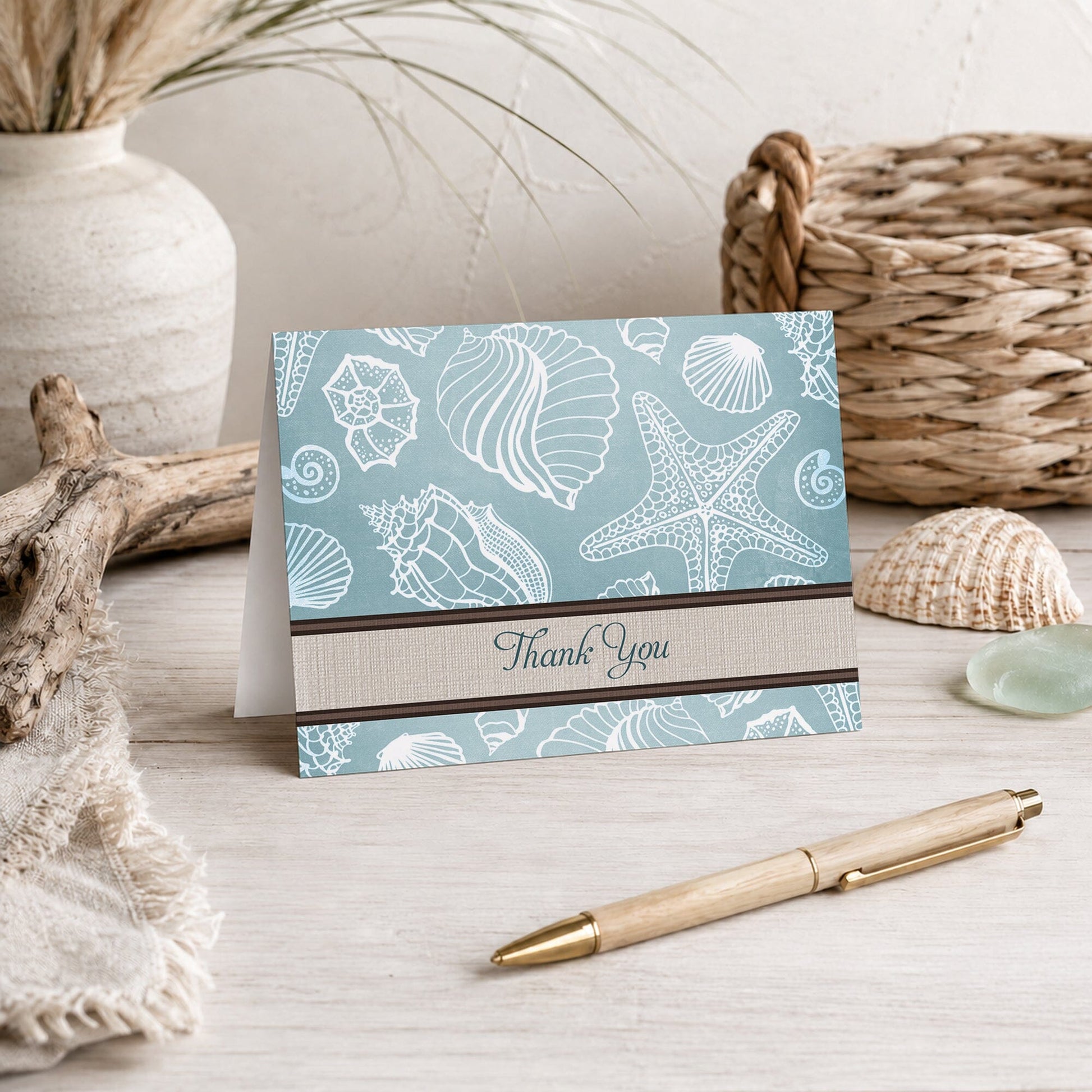 Rustic Beach Linen Seashell Thank You Card shown on a beach house tabletop with coastal decor and a pen.