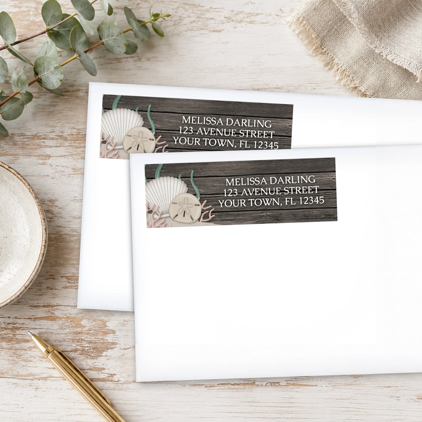 Rustic Beach Seashells and Wood Address Labels on white envelopes, shown on a wooden surface with plants and a pen.