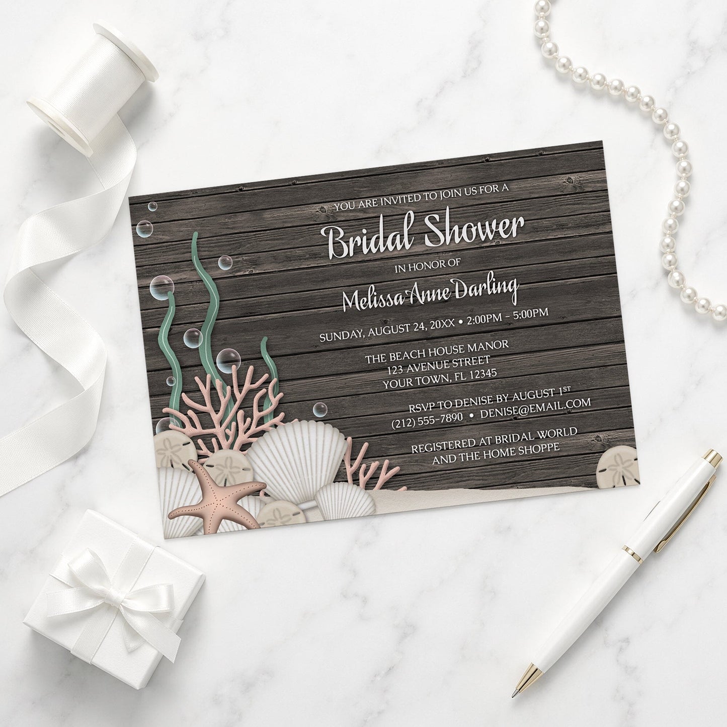 Rustic Beach Seashells and Wood Bridal Shower Invitation on a marble surface with a gift box and pen.