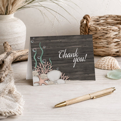 Rustic Beach Seashells and Wood Thank You Card shown on a beach house tabletop with coastal decor, vase, and a pen.