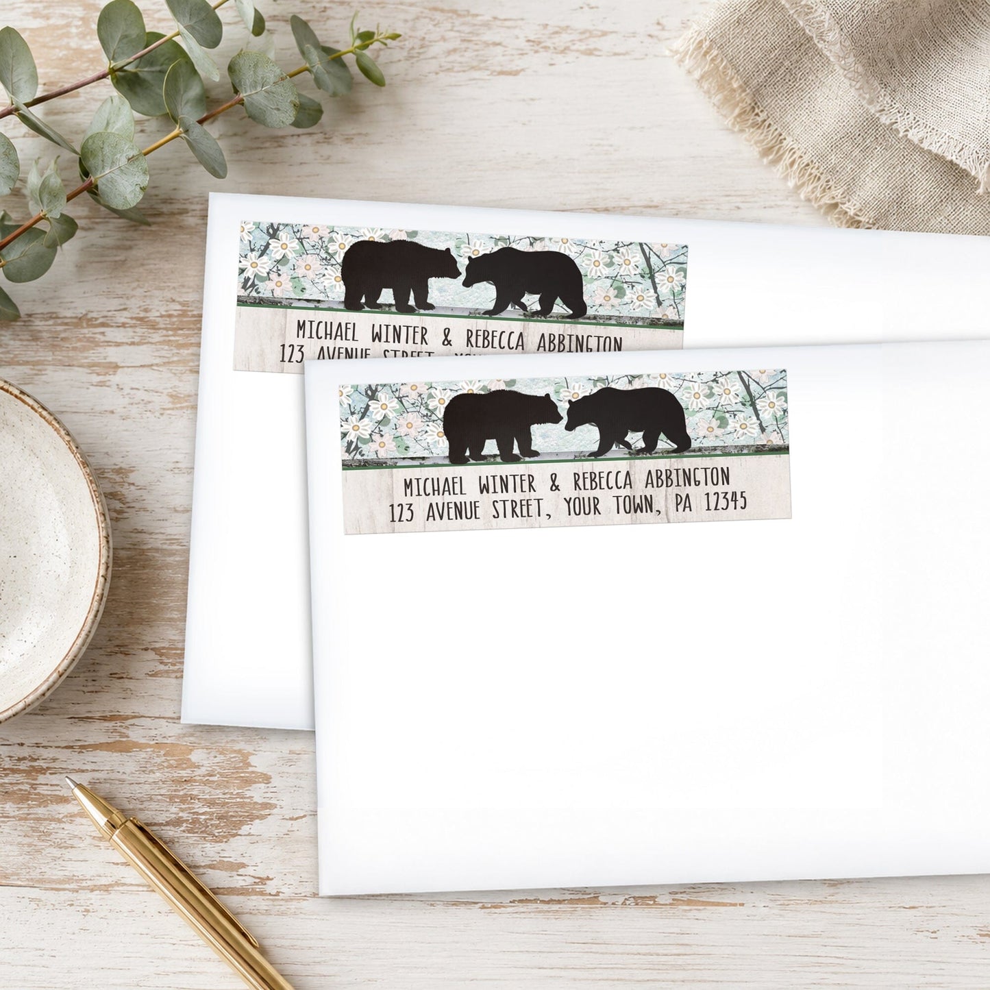 Rustic Bear Floral Wood Address Labels on white envelopes on a wooden surface with plants and a pen.
