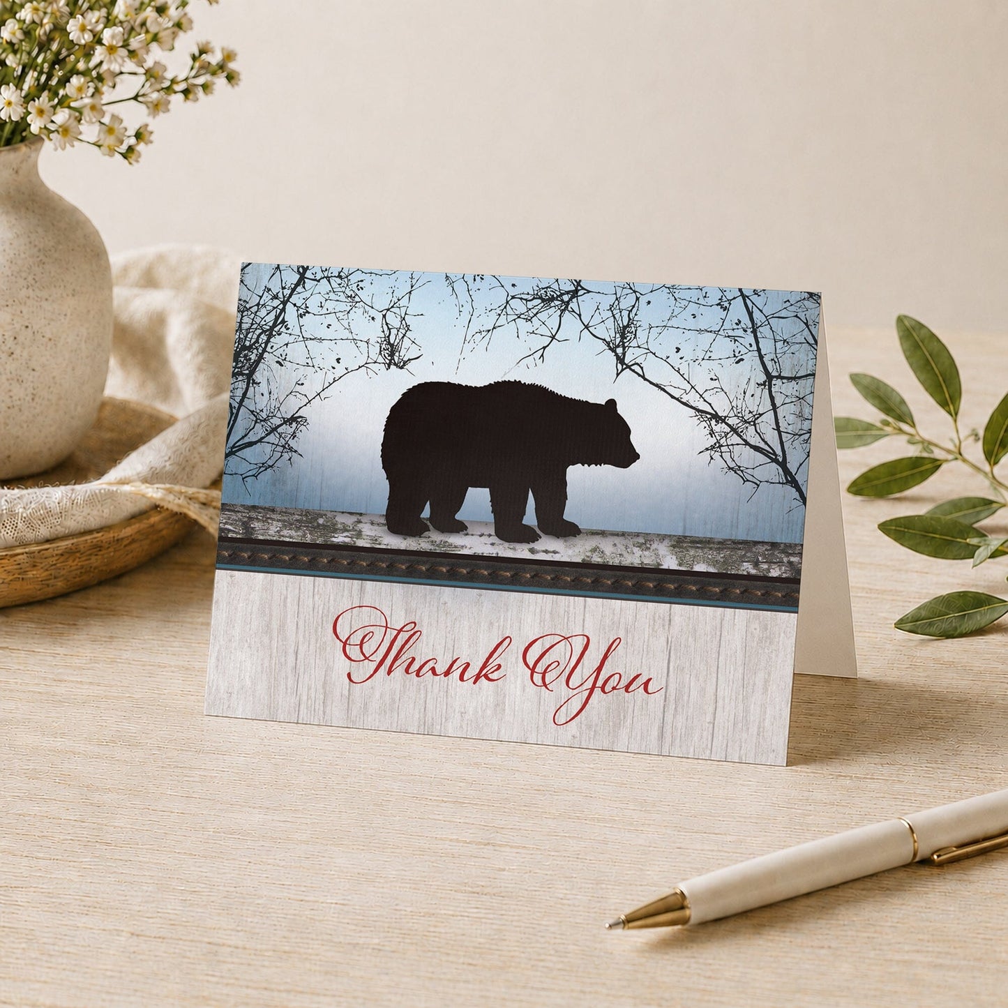 Rustic Bear Wood Red Blue Thank You Card shown on a desk with a vase, plants, and a pen.