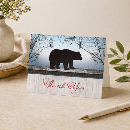 Rustic Bear Wood Red Blue Thank You Card shown on a desk with a vase, plants, and a pen.