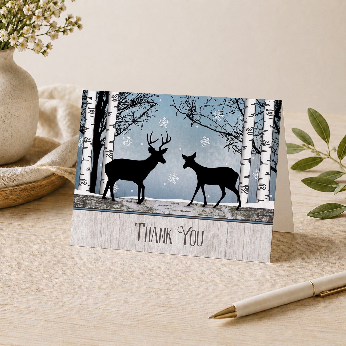 Rustic Blue Winter Deer Thank You Card shown on a desk with a vase, plants, and a pen.