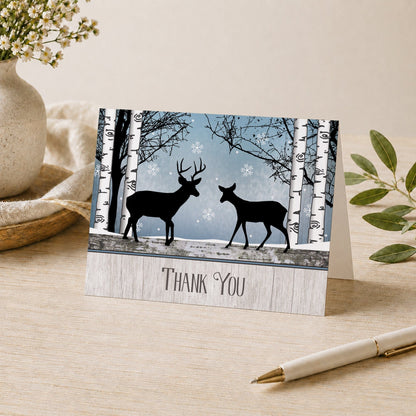 Rustic Blue Winter Deer Thank You Card shown on a desk with a vase, plants, and a pen.
