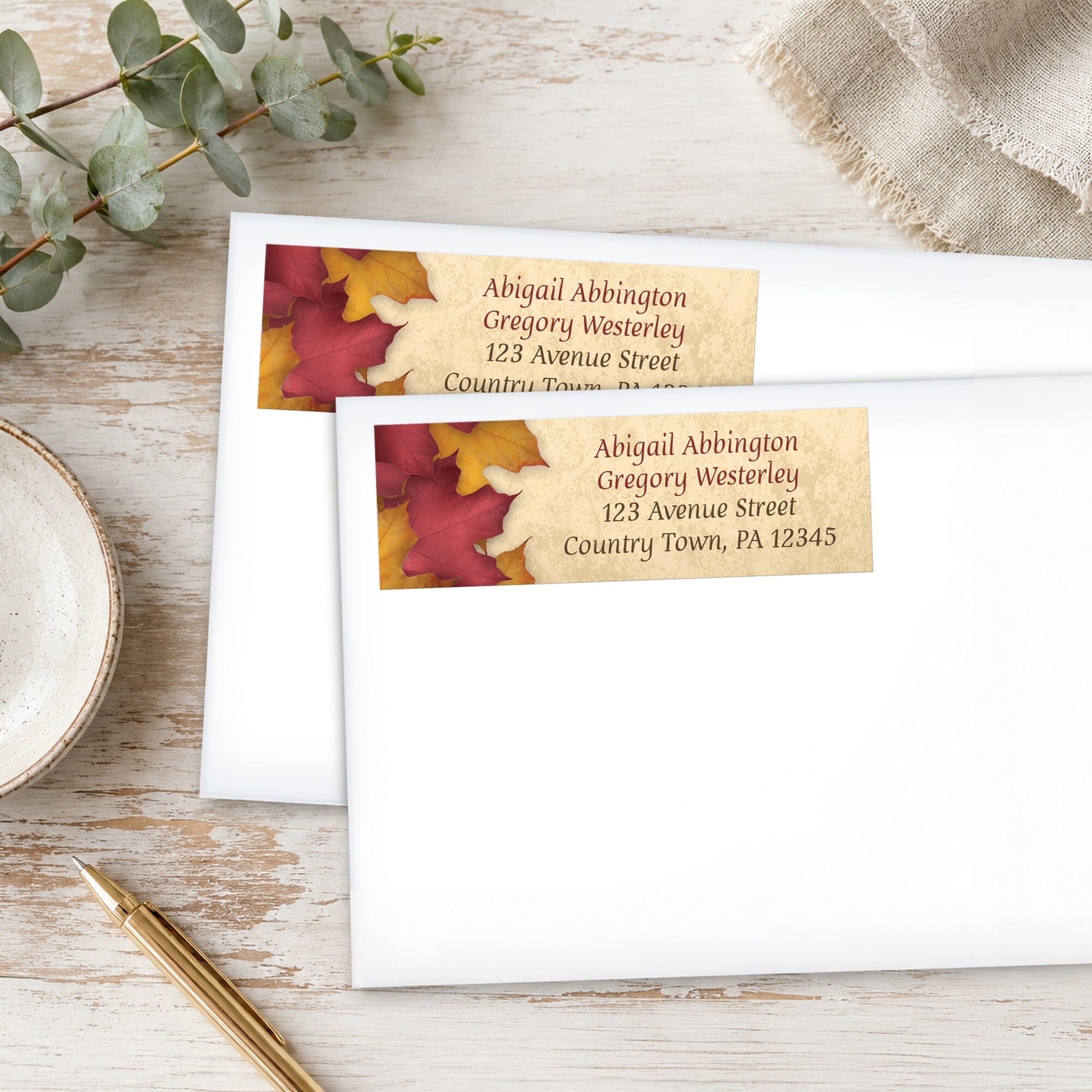 Rustic Burgundy Gold Autumn Address Labels with fall leaf design, shown on white envelopes, with a pen and eucalyptus branch on a wooden surface.