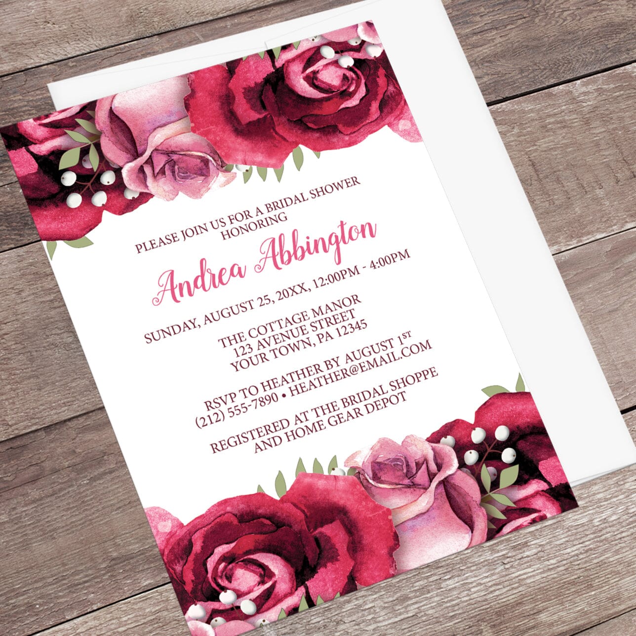Bridal shower invitation with burgundy and pink roses, shown at an angle with an envelope on a wooden surface