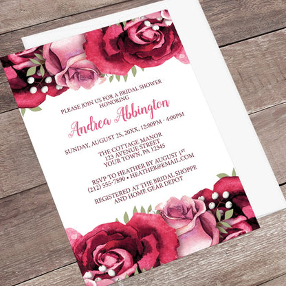 Bridal shower invitation with burgundy and pink roses, shown at an angle with an envelope on a wooden surface