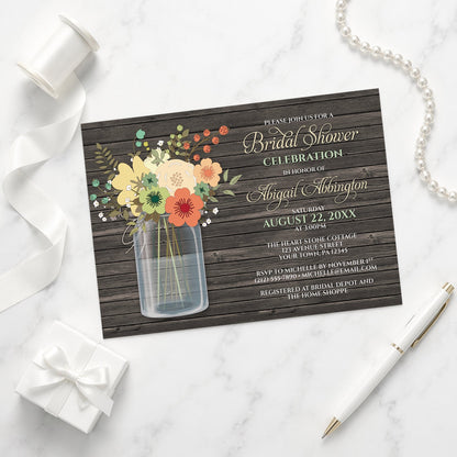 Rustic Floral Wood Mason Jar Bridal Shower Invitation on a marble surface with white ribbon, gift box, pen, and a pearl necklace.