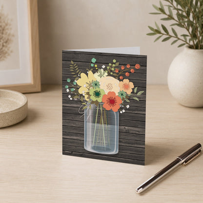 Rustic Floral Wood Mason Jar Note Card shown on a desk with a vase and pen.