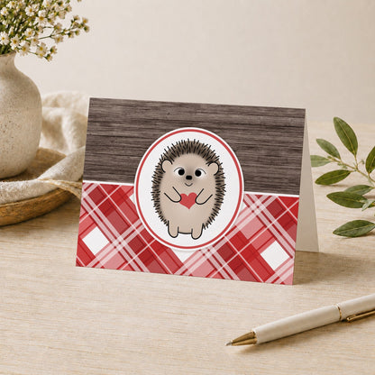 Rustic Hedgehog Heart Red Plaid Note Card shown on a tabletop with a vase, plants, and a pen.