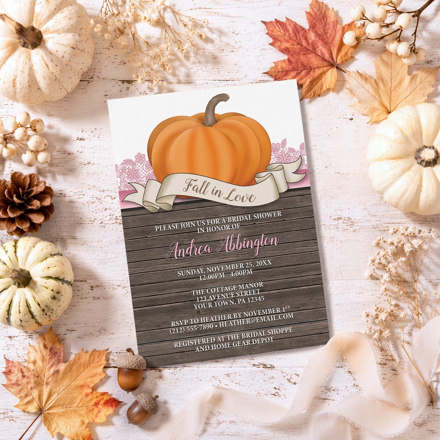 Rustic Orange Pink Pumpkin Fall in Love Bridal Shower Invitation surrounded by autumn decorations on a wooden surface.