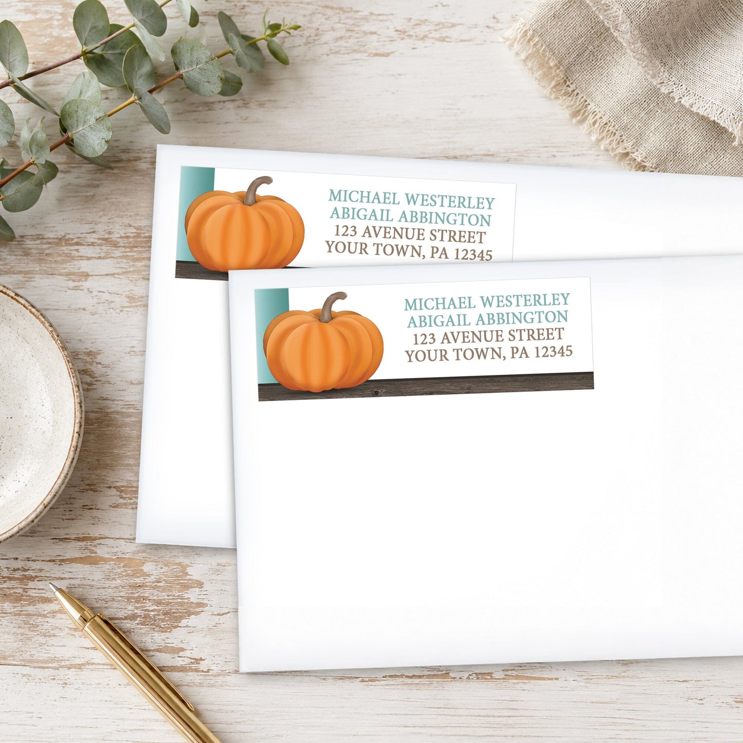 Rustic Orange Teal Pumpkin Address Labels on white envelopes, shown on a wooden surface with eucalyptus leaves and a pen.