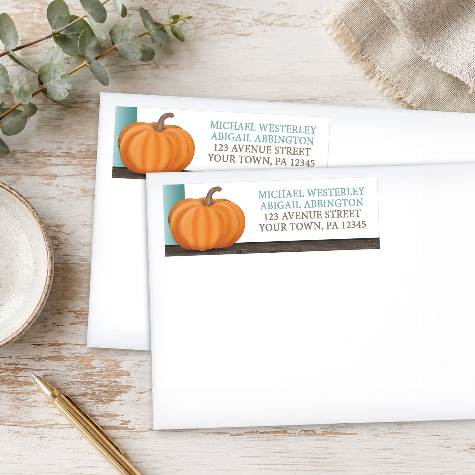 Rustic Orange Teal Pumpkin Address Labels on white envelopes, shown on a wooden surface with eucalyptus leaves and a pen.