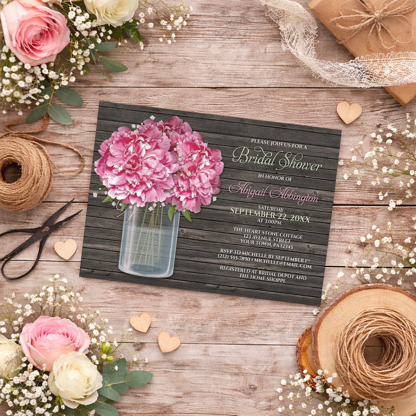 Rustic Peony Wood Mason Jar Bridal Shower Invitation with a pink flowers design, shown on a wooden surface with spring and summer flowers, wooden hearts, and ribbons.