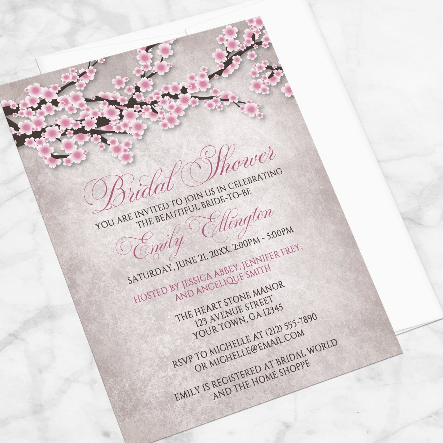 Bridal shower invitation with a rustic pink cherry blossom design, displayed at an angle with a white envelope on a marble surface