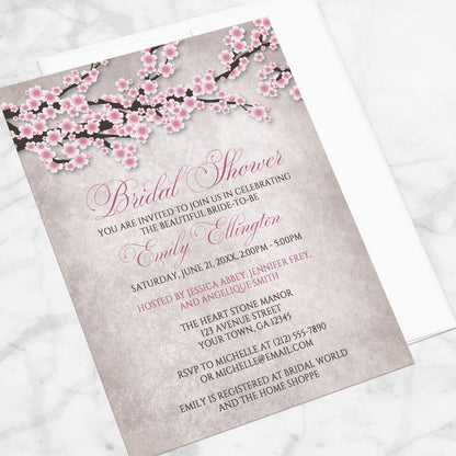 Bridal shower invitation with a rustic pink cherry blossom design, displayed at an angle with a white envelope on a marble surface