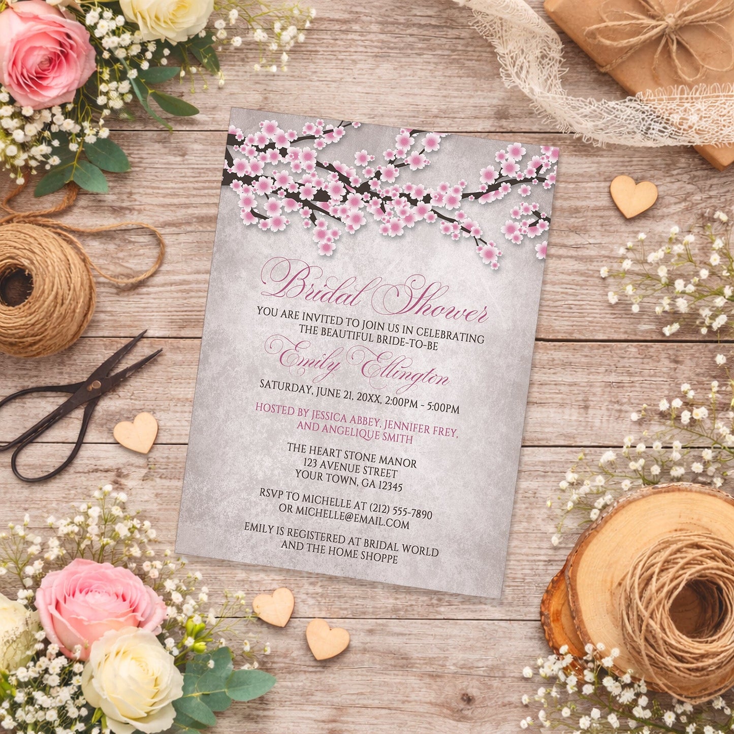 Rustic Pink Cherry Blossom Bridal Shower Invitation on a wooden surface with spring and summer flowers and twine.