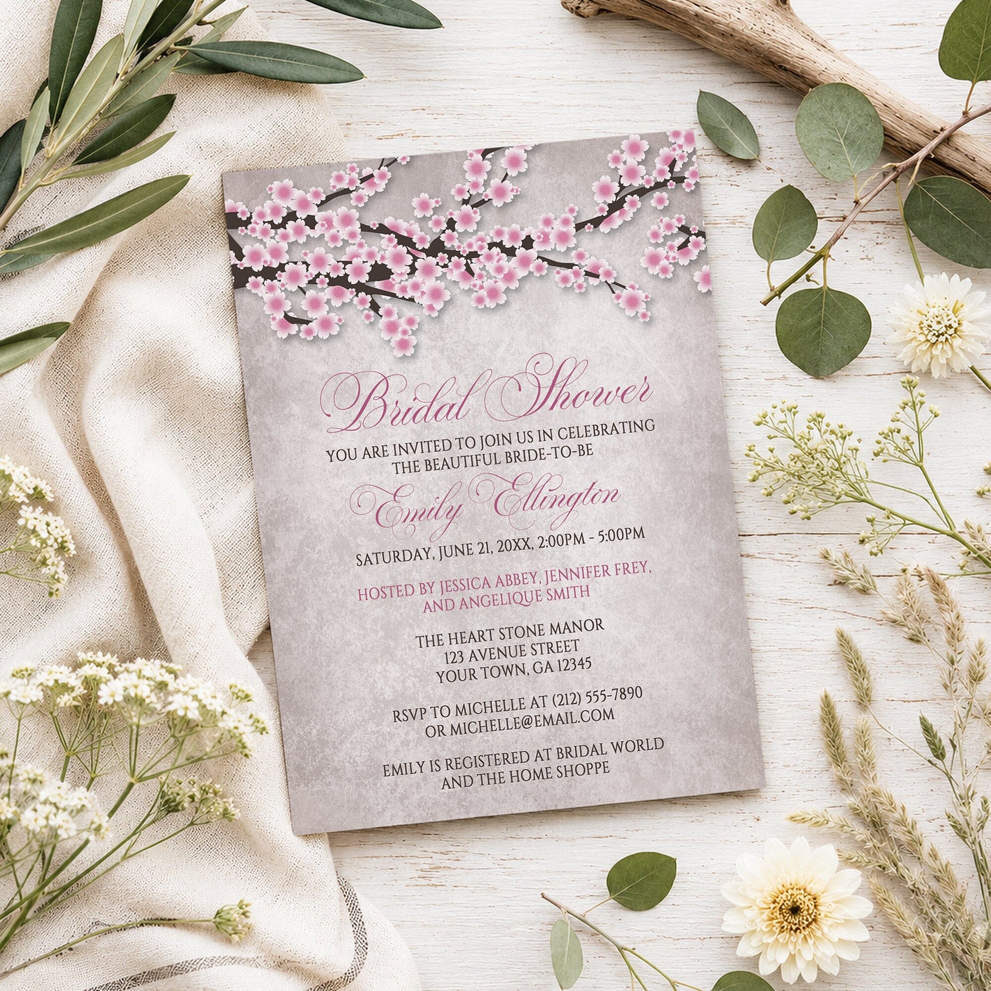 Rustic Pink Cherry Blossom Bridal Shower Invitation shown on a light wooden surface with spring and summer plants.
