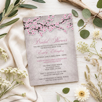 Rustic Pink Cherry Blossom Bridal Shower Invitation shown on a light wooden surface with spring and summer plants.