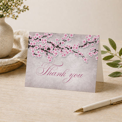 Rustic Pink Cherry Blossom Thank You Card on a desk with a vase, plants, and a pen.