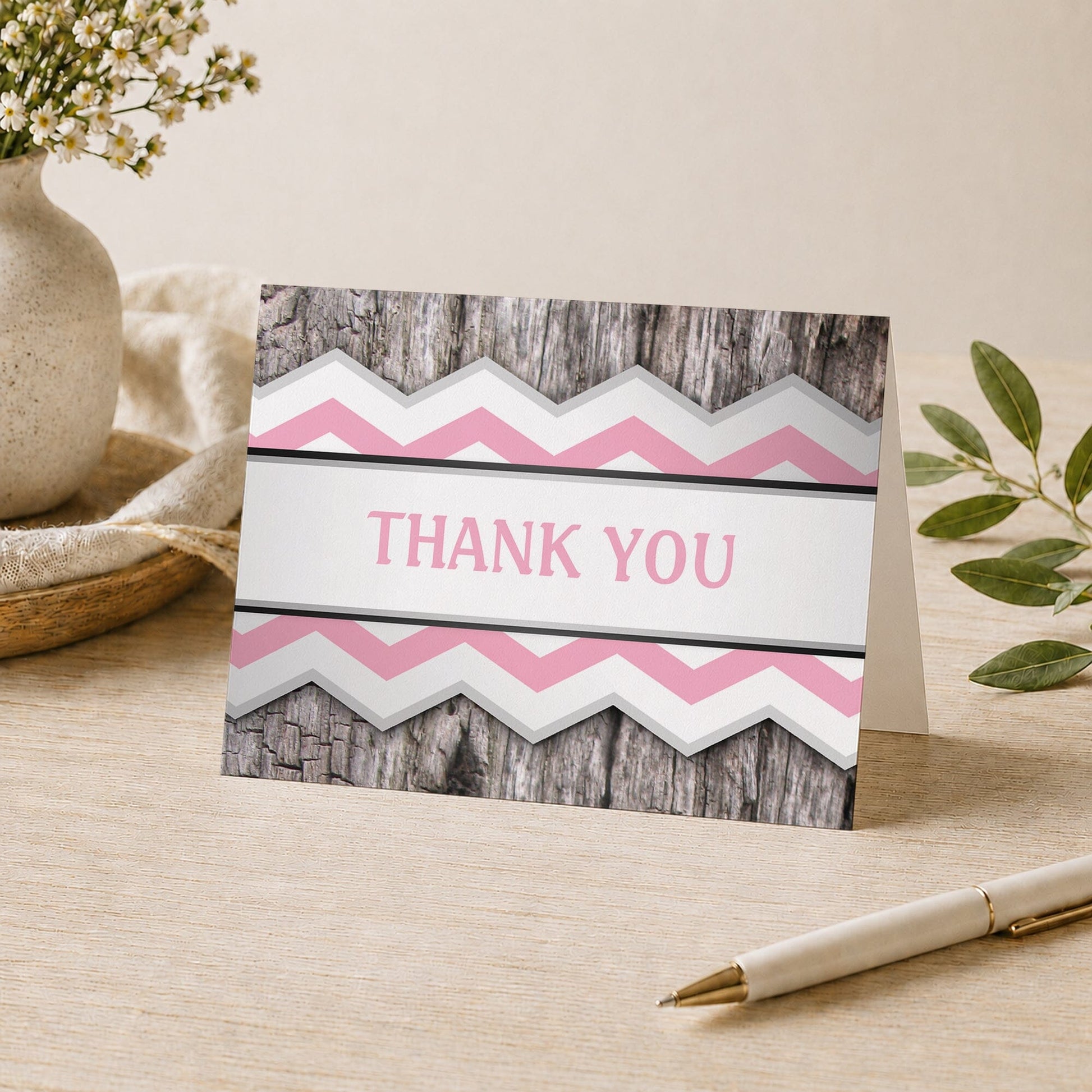 Rustic Pink Chevron and Wood Thank You Card shown on a desk with a vase, plants, and a pen.