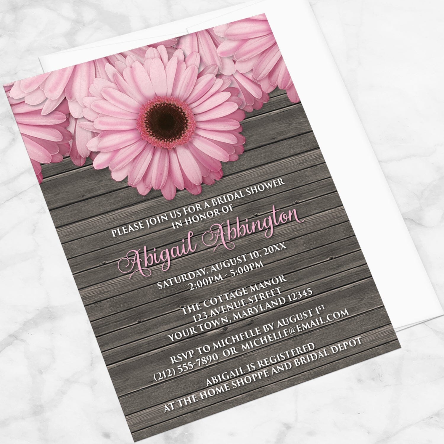 Rustic Pink Daisy Brown Wood Bridal Shower Invitation shown at an angle on a marble surface with a white envelope.