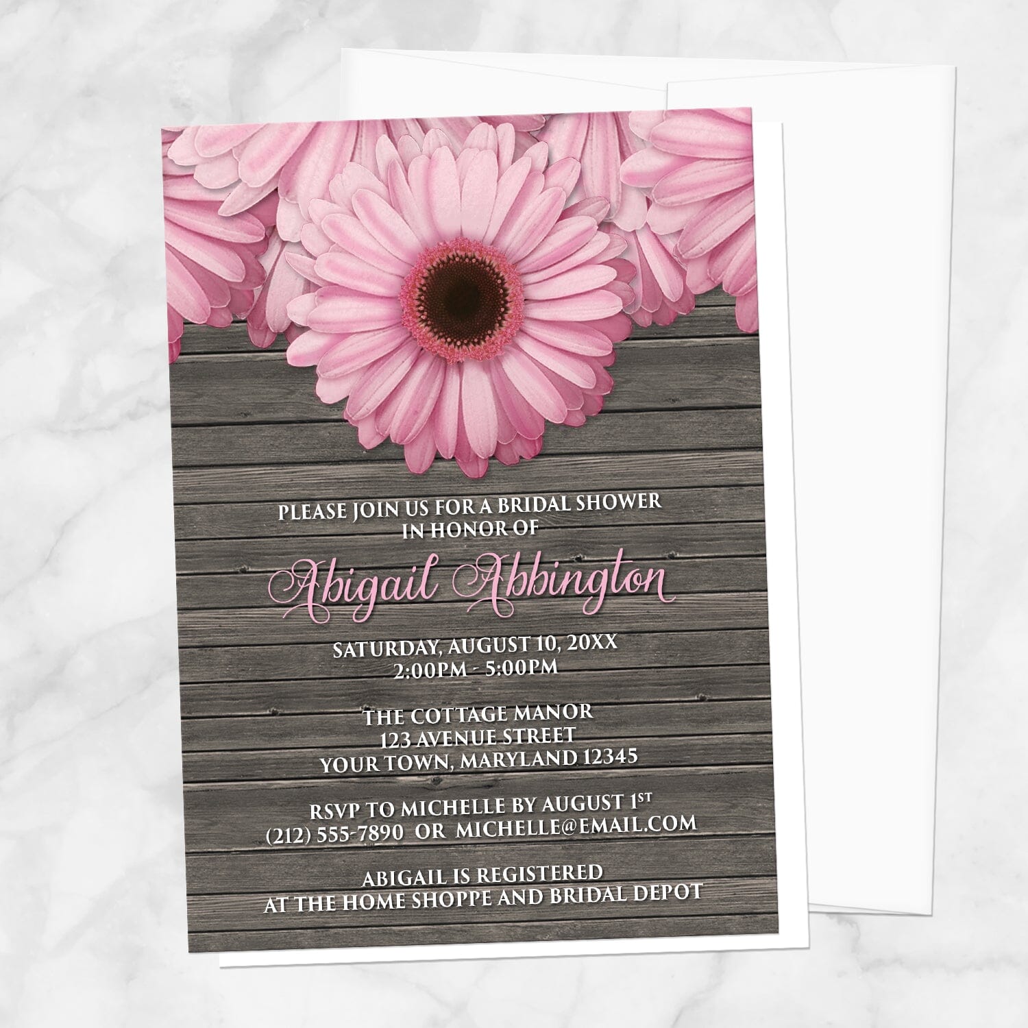 Rustic Pink Daisy Brown Wood Bridal Shower Invitation shown on a marble surface with a white envelope.