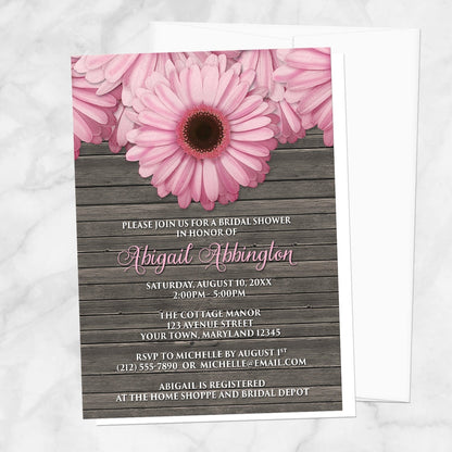 Rustic Pink Daisy Brown Wood Bridal Shower Invitation shown on a marble surface with a white envelope.
