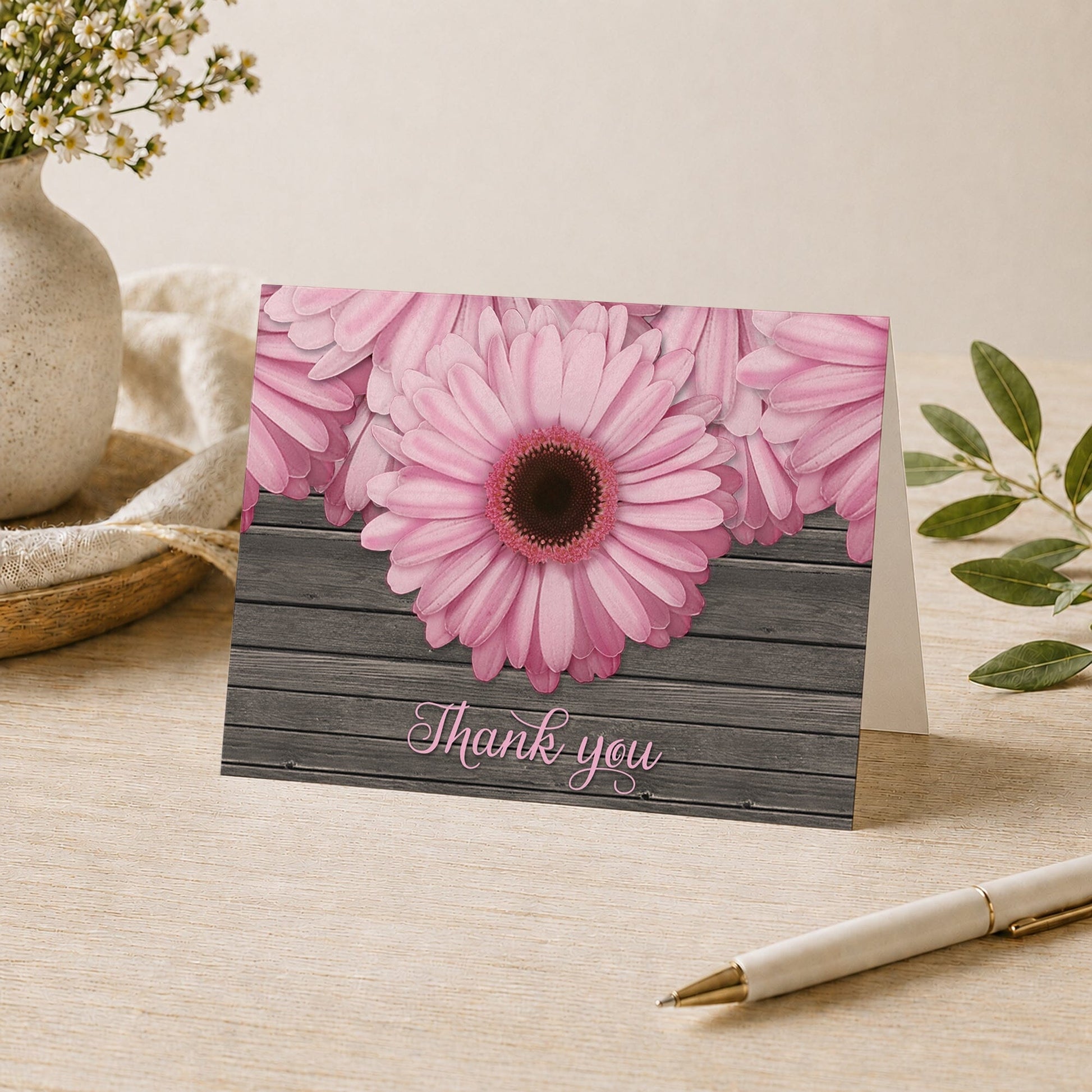 Rustic Pink Daisy Brown Wood Thank You Card shown on a desk with a vase, plants, and a pen.