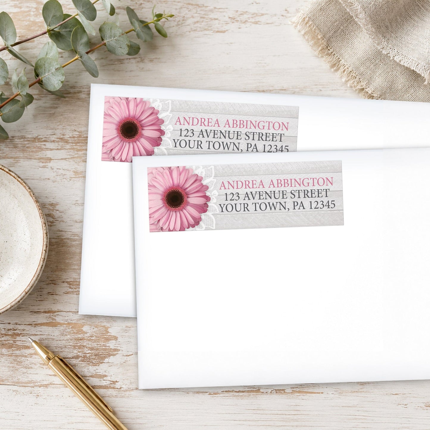 Rustic Pink Daisy Gray Wood Address Labels, shown on white envelopes, on a wooden surface with eucalyptus leaves and a pen.