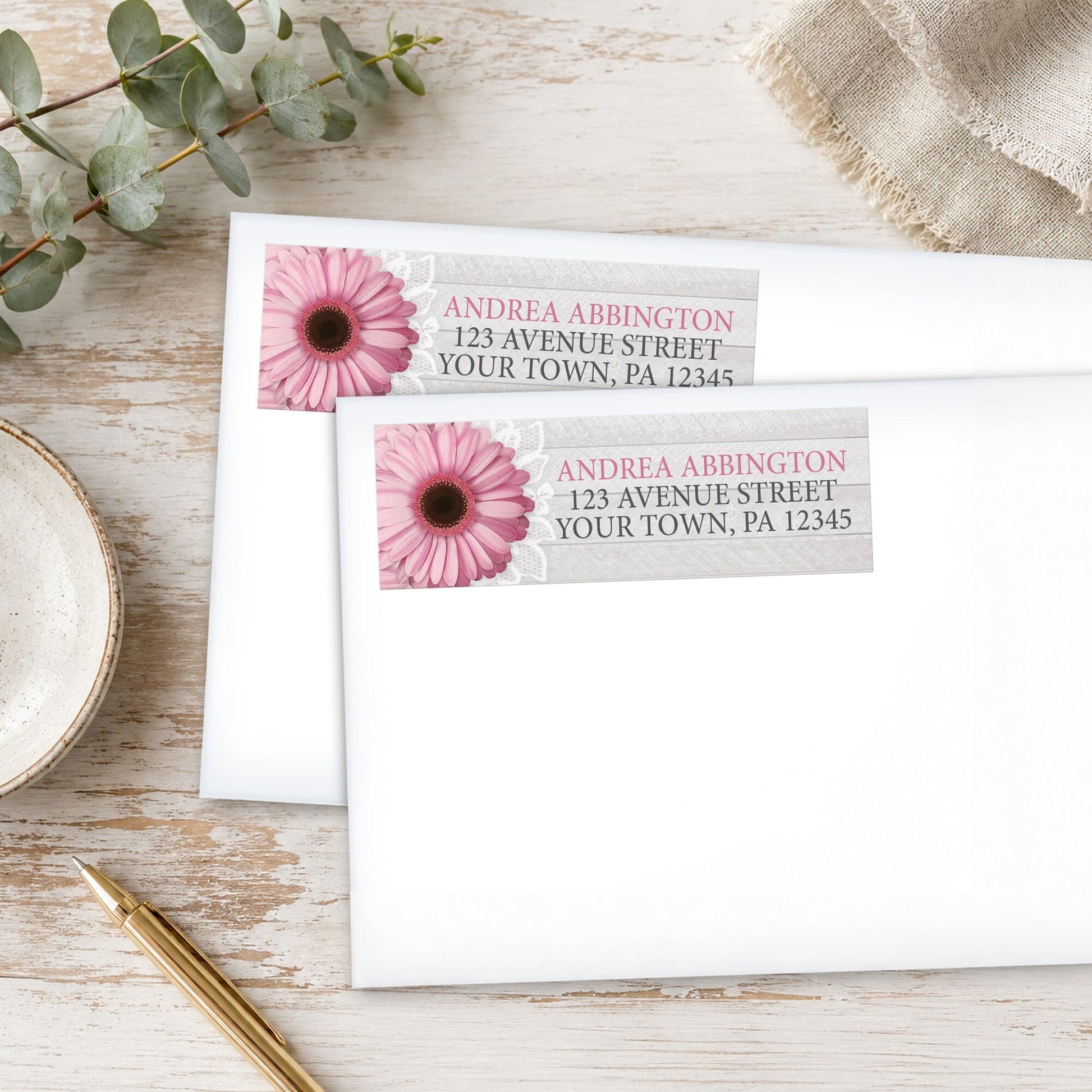 Rustic Pink Daisy Gray Wood Address Labels, shown on white envelopes, on a wooden surface with eucalyptus leaves and a pen.