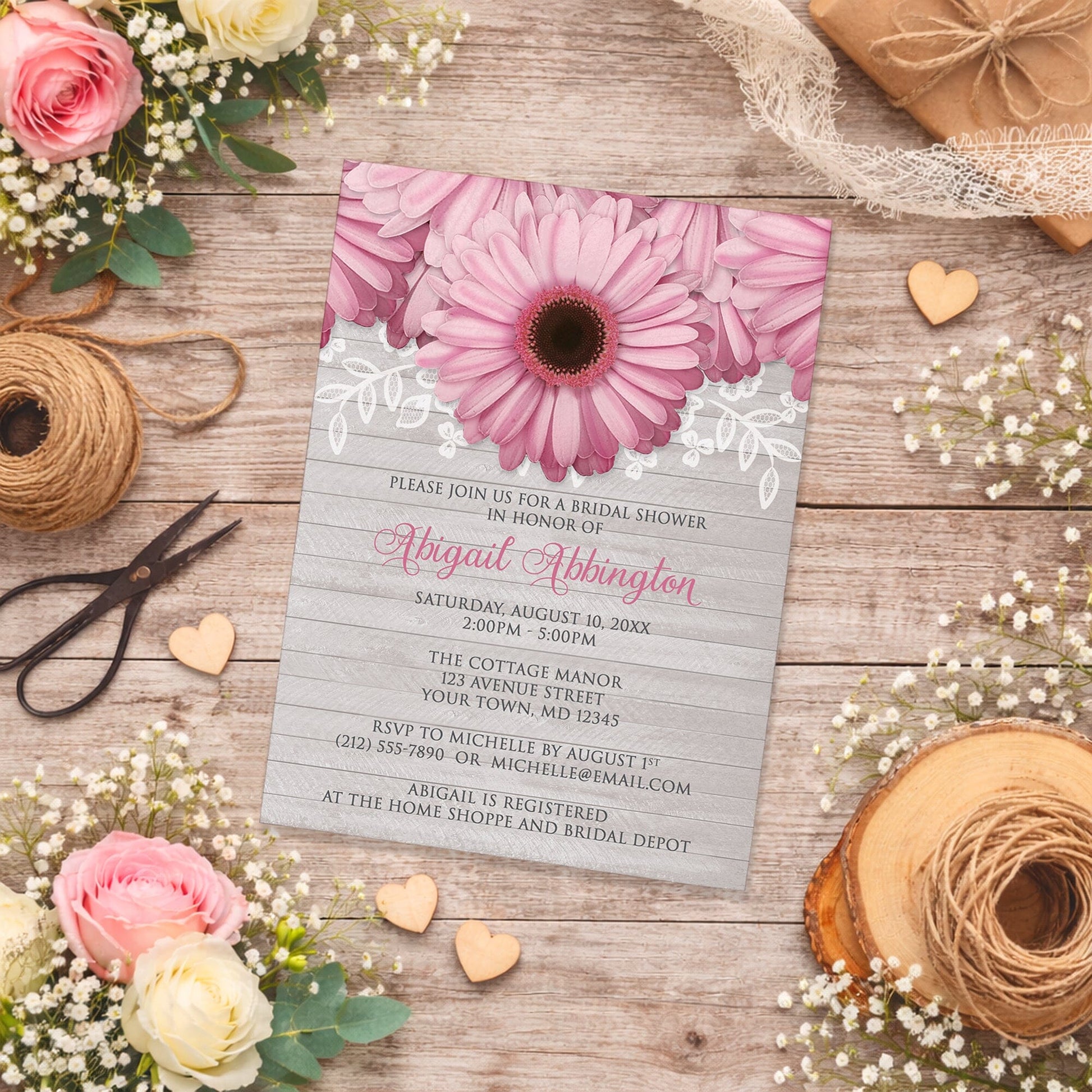 Rustic Pink Daisy Gray Wood Bridal Shower Invitation on a wooden surface with spring and summer flowers, wooden hearts, and twine.