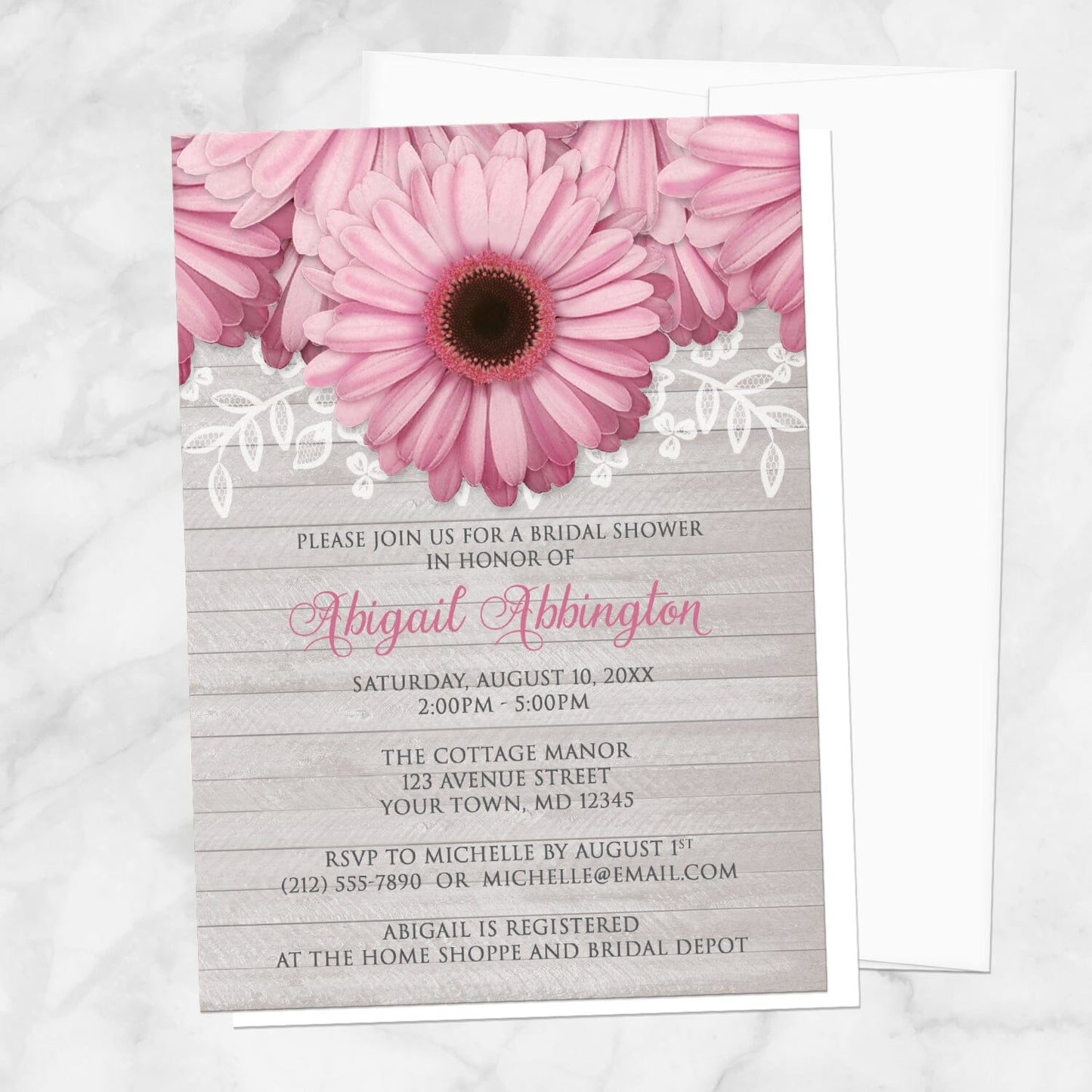 Bridal shower invitation with pink daisies, white lace, and soft gray wood, displayed with a white envelope on a marble surface