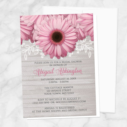 Bridal shower invitation with pink daisies, white lace, and soft gray wood, displayed with a white envelope on a marble surface