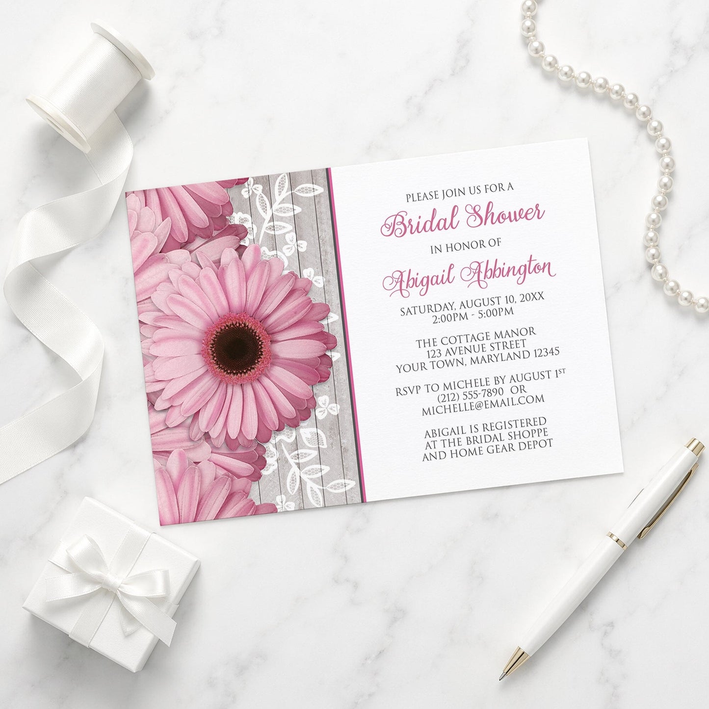 Rustic Pink Daisy Wood White Bridal Shower Invitation shown on a marble surface with a white gift box, pen, ribbon, and pearls.