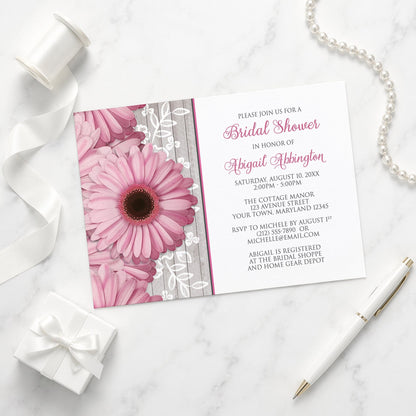 Rustic Pink Daisy Wood White Bridal Shower Invitation shown on a marble surface with a white gift box, pen, ribbon, and pearls.