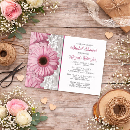 Rustic Pink Daisy Wood White Bridal Shower Invitation shown on a country wood surface with spring and summer flowers, small wood hearts, lace ribbon, and twine.