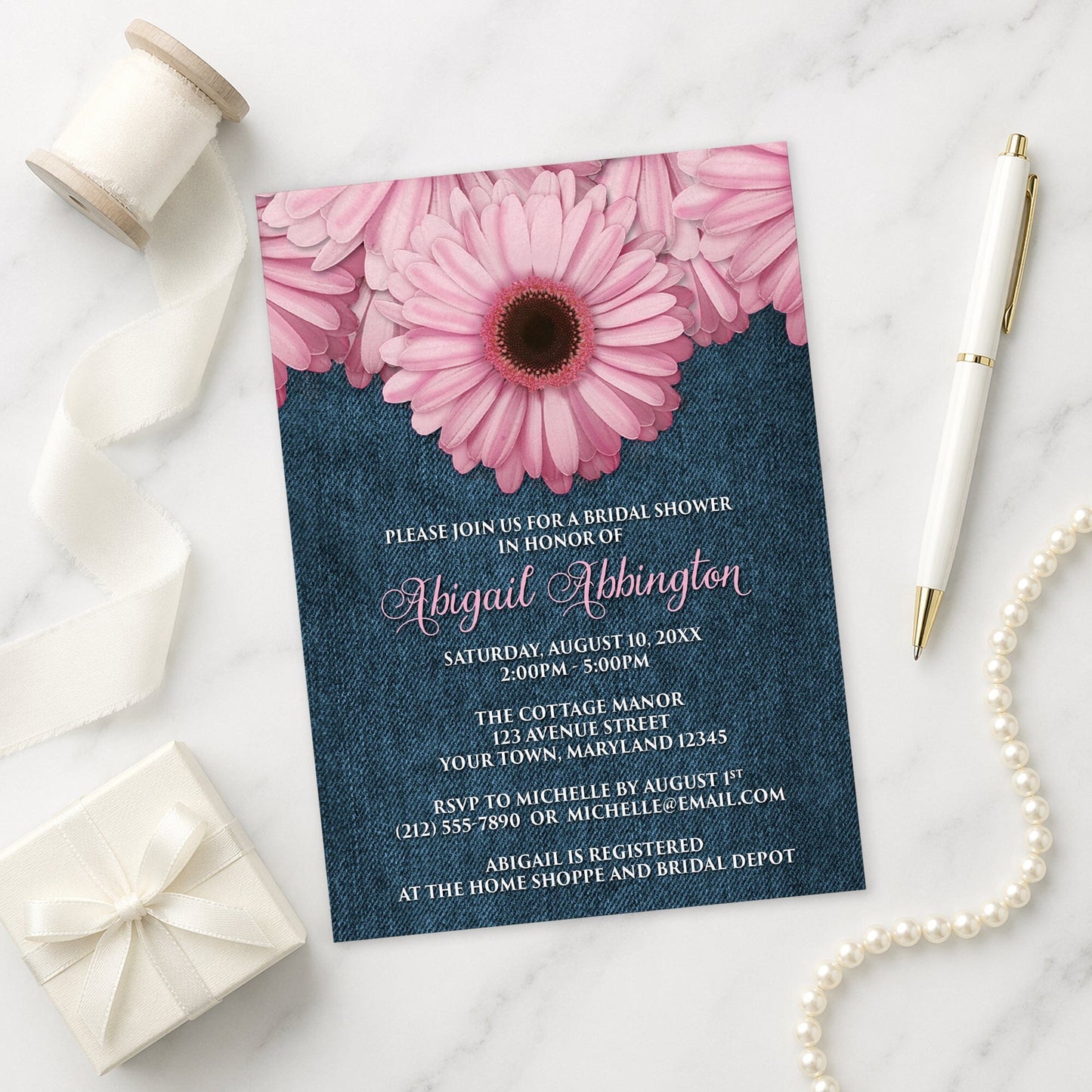 Rustic Pink Daisy and Denim Bridal Shower Invitation shown on a marble surface with a white gift box, pen, ribbon, and pearls.