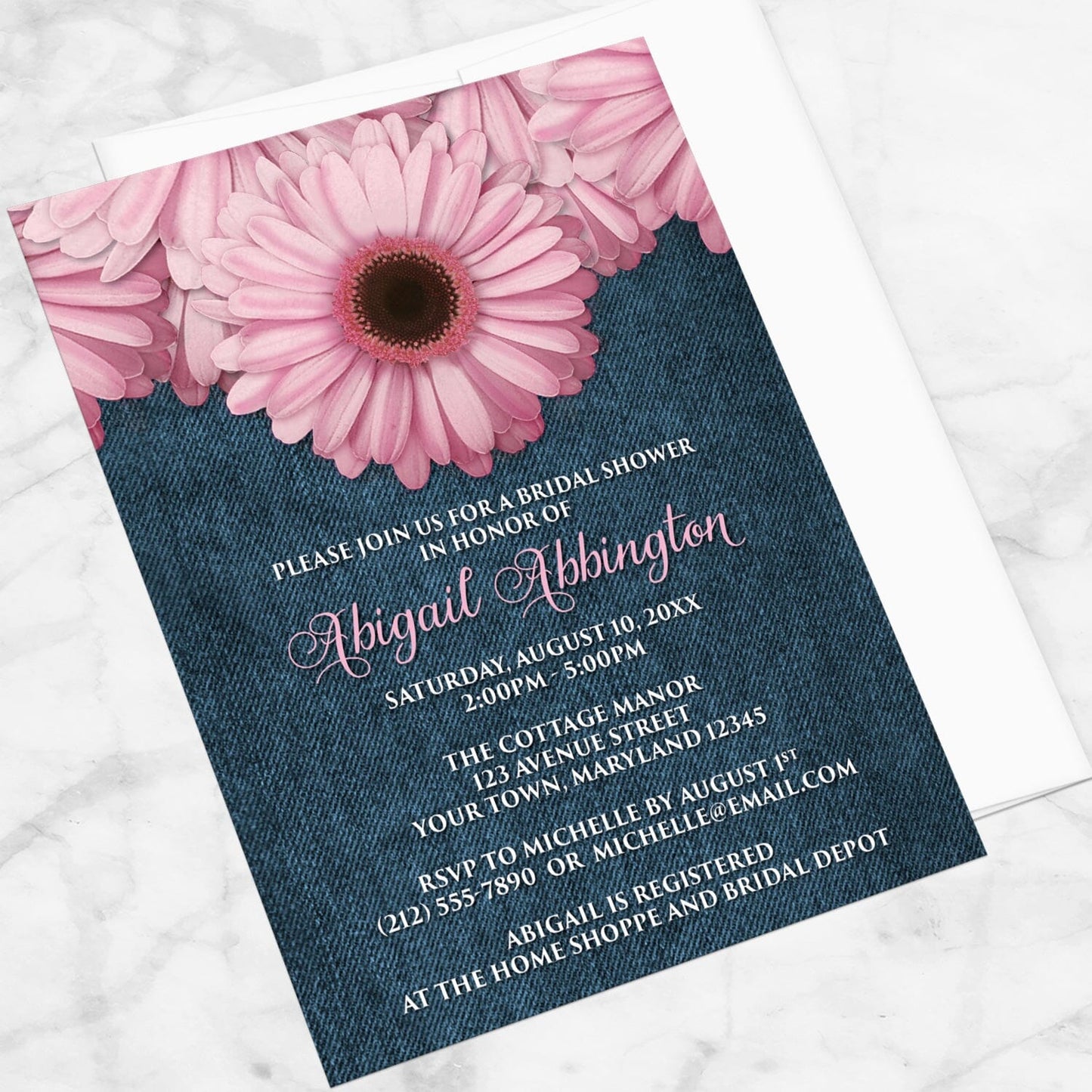 Rustic Pink Daisy and Denim Bridal Shower Invitation shown at an angle on a marble surface with a white envelope.
