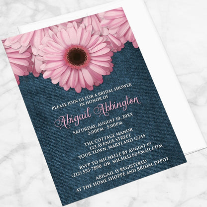 Rustic Pink Daisy and Denim Bridal Shower Invitation shown at an angle on a marble surface with a white envelope.