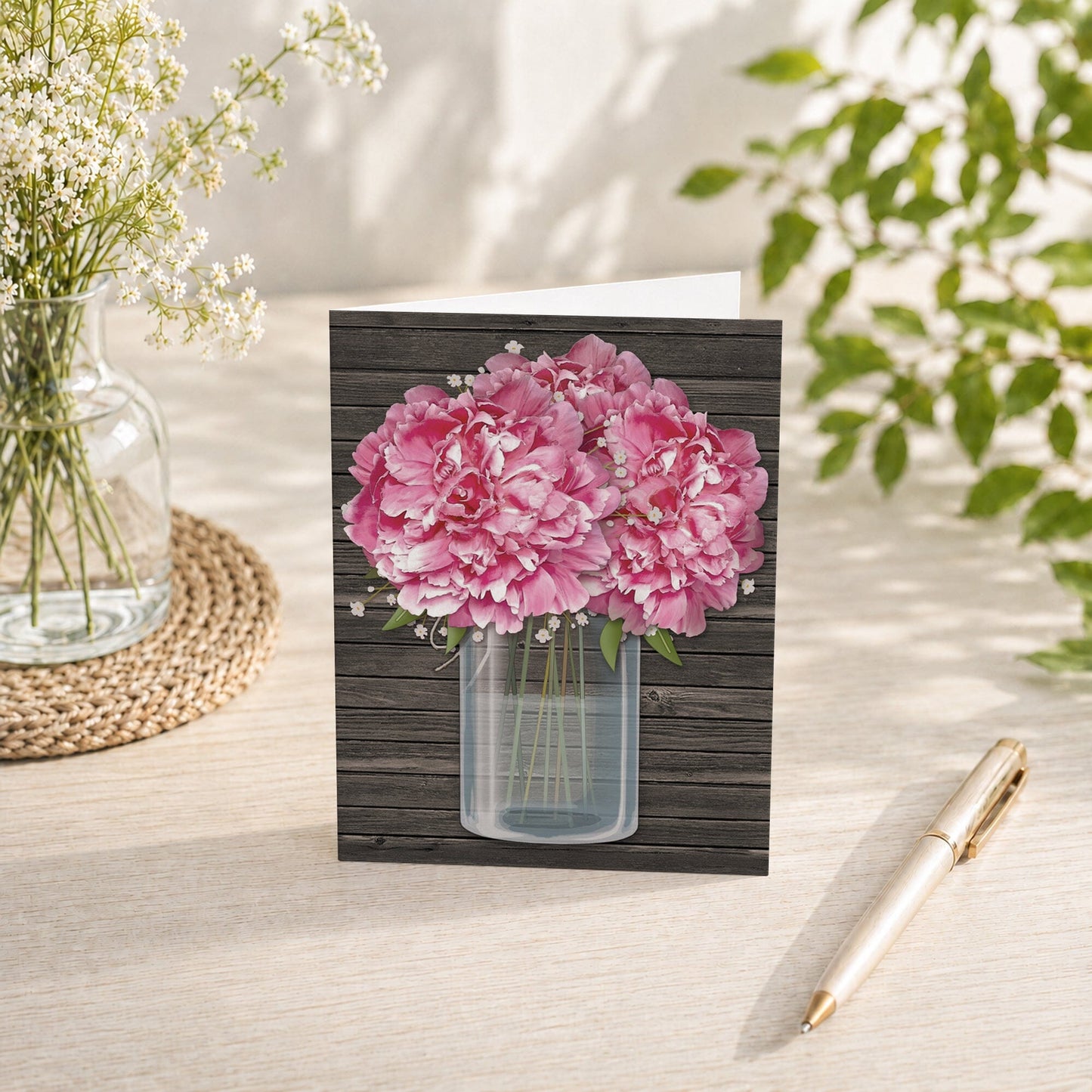Rustic Pink Peony Wood Mason Jar Note Card shown on a tabletop with a vase, spring and summer flowers and plants, and a pen.