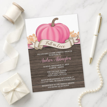 Rustic Pink Pumpkin Fall in Love Bridal Shower Invitation shown on a marble surface with a white gift box, pen, ribbon, and pearls.