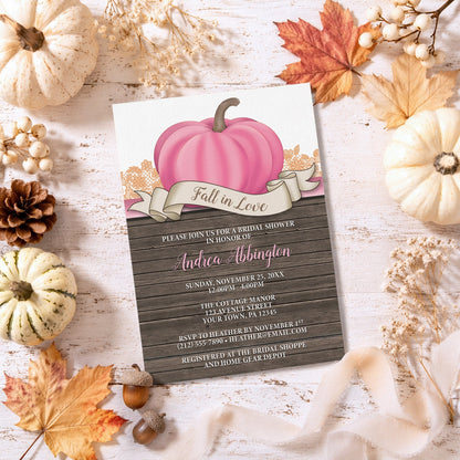 Rustic Pink Pumpkin Fall in Love Bridal Shower Invitation shown on a light wooden surface with autumn decor.
