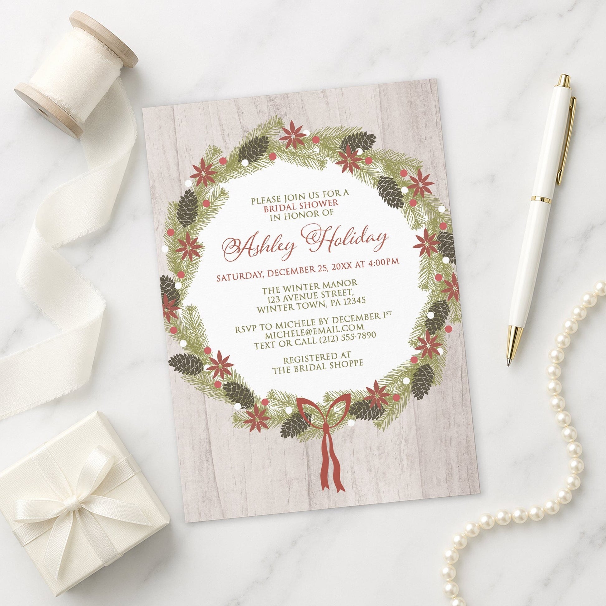 Rustic Poinsettia Pine Cone Wreath Bridal Shower Invitation on a marble surface with a white gift box, pen, ribbon, and pearls.
