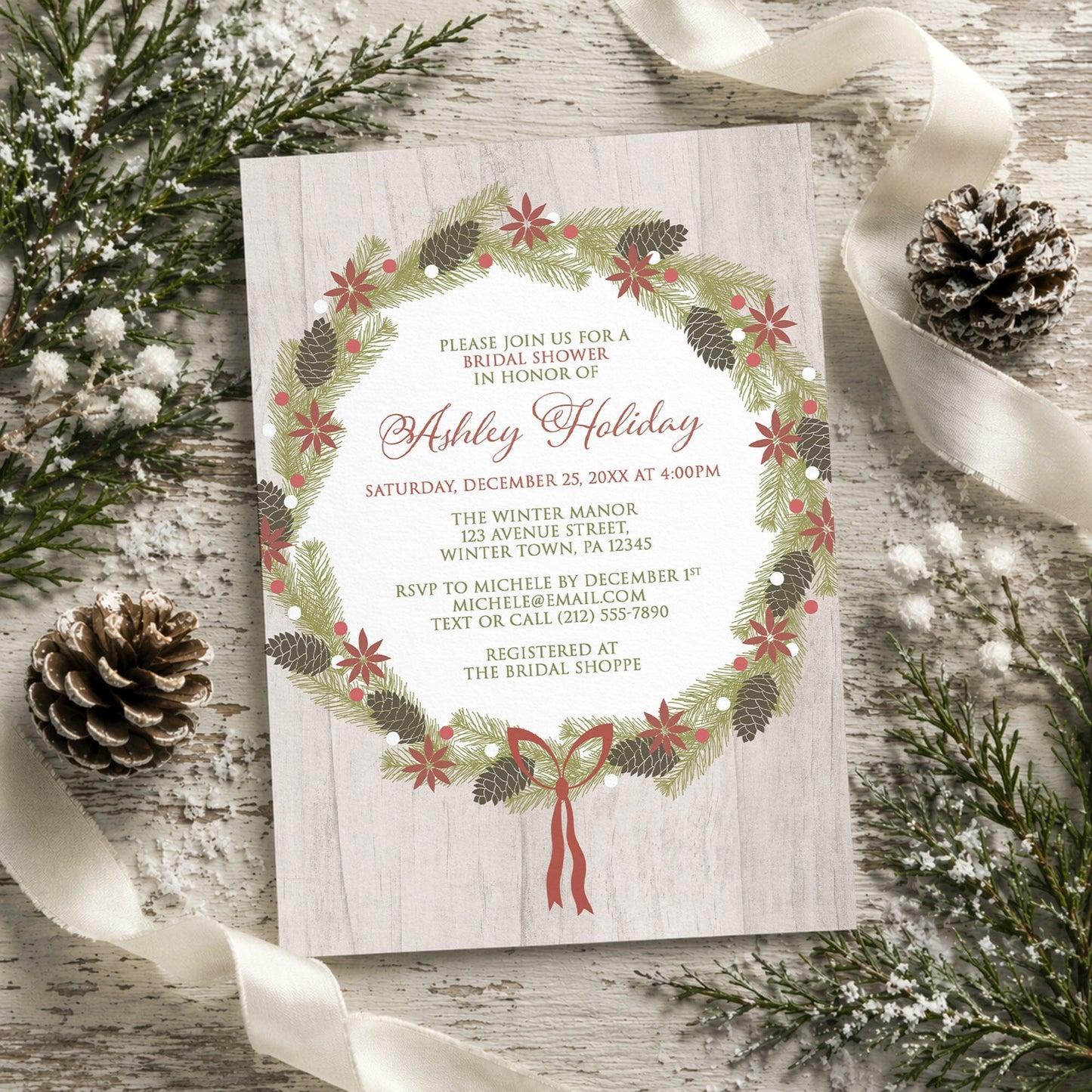 Rustic Poinsettia Pine Cone Wreath Bridal Shower Invitation on a rustic wood surface with winter pine cones and ribbon.