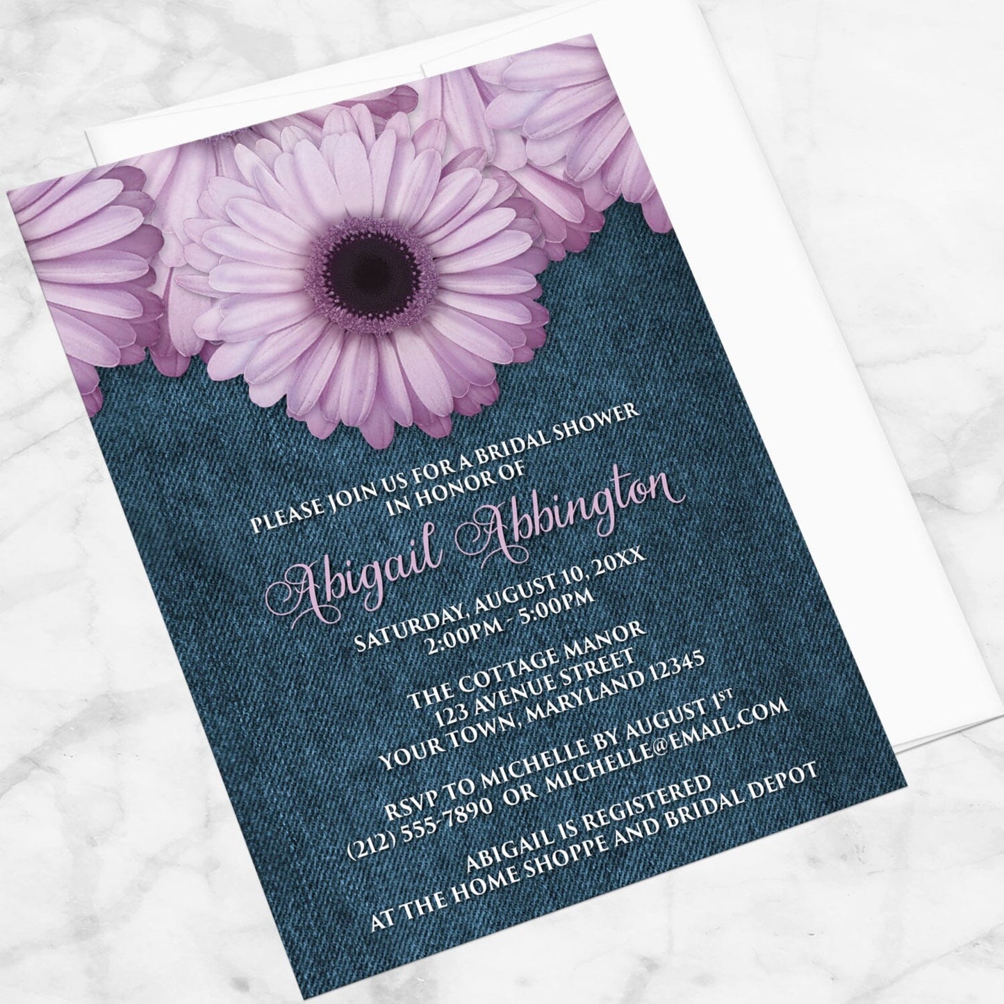 Rustic Purple Daisy Denim Bridal Shower Invitation shown at an angle on a marble surface with a white envelope.