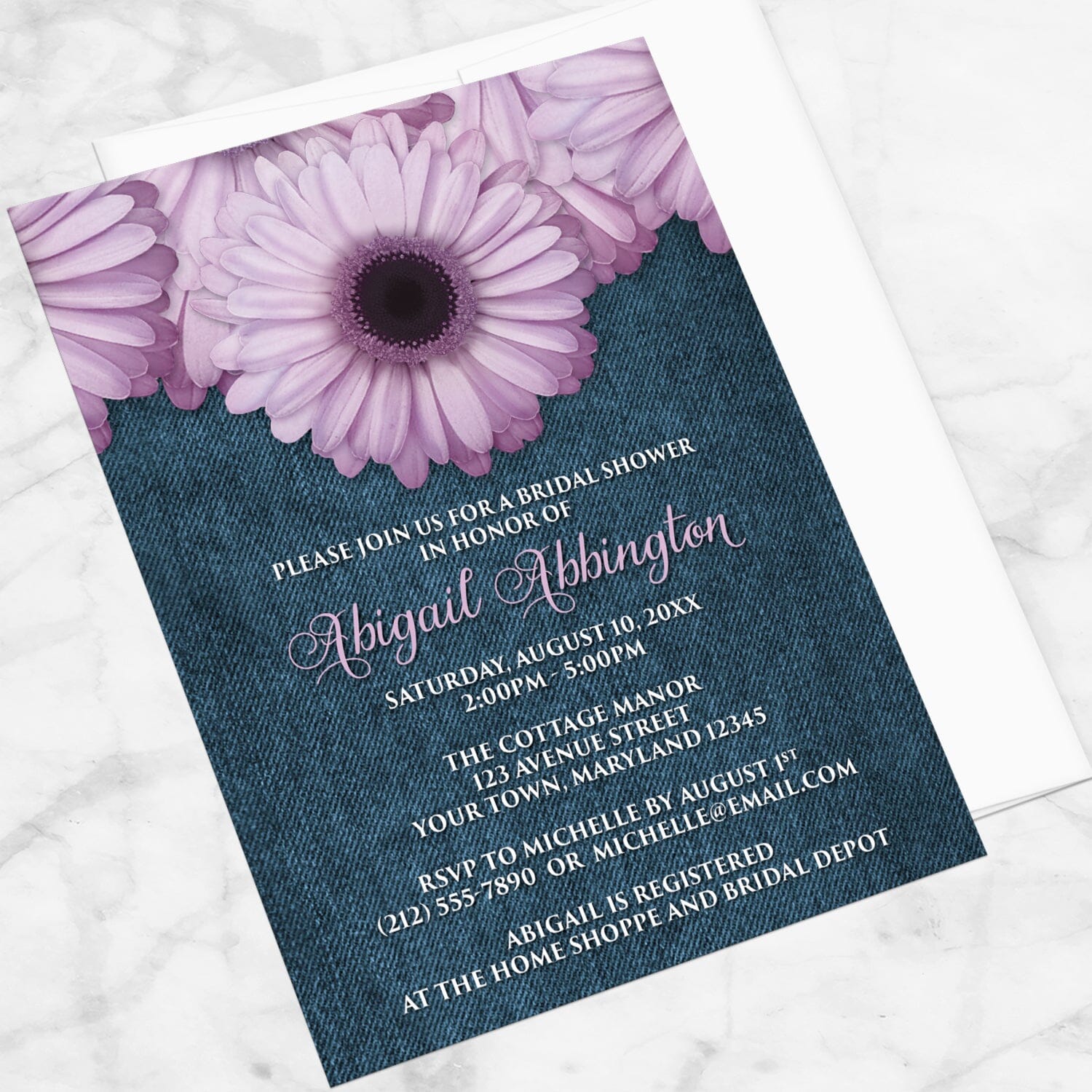 Rustic Purple Daisy Denim Bridal Shower Invitation shown at an angle on a marble surface with a white envelope.